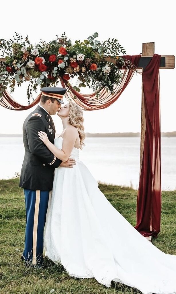 Military couple kiss on their wedding day by their altar. Fall altar flowers with draping.